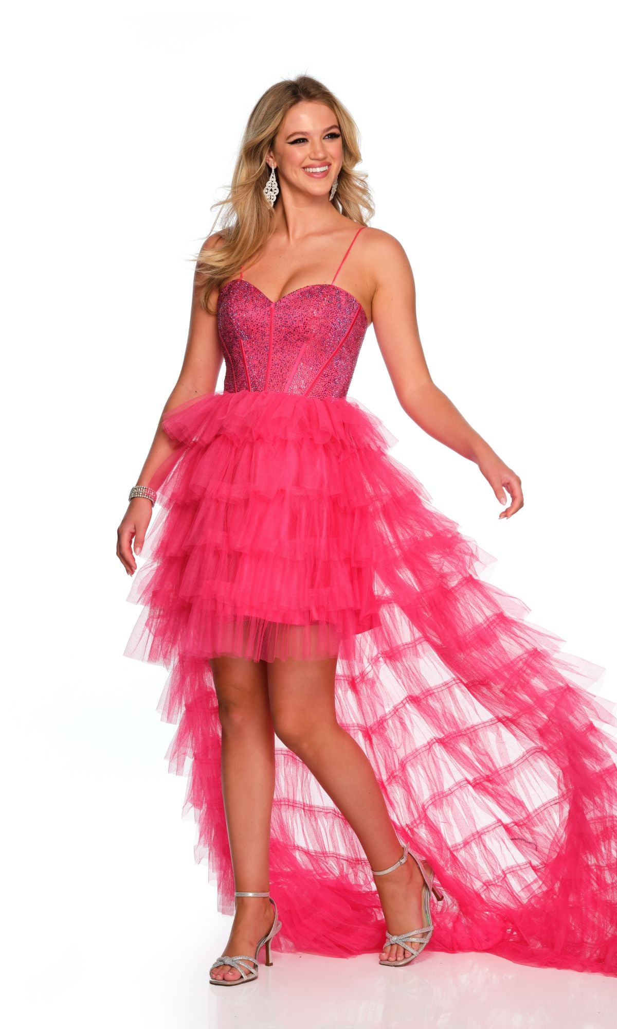 A woman stands smiling in silver heels against a white backdrop, wearing the Dave and Johnny Pink High-Low Prom Dress 11174 featuring a fuchsia ruffled skirt and an embellished corset bodice.